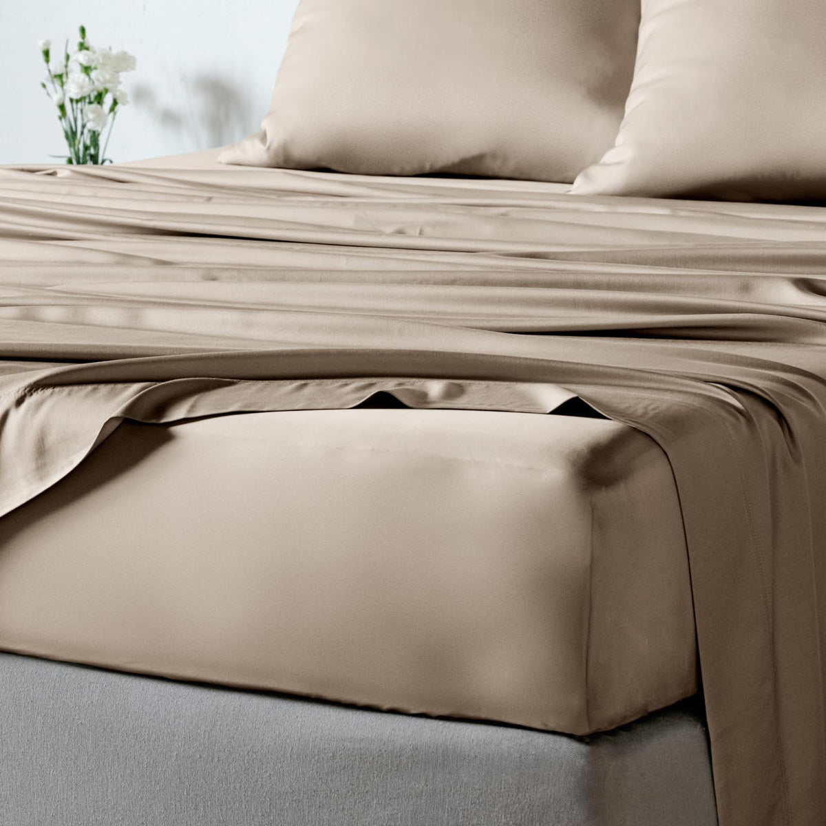 Taupe bamboo sheet set on a bed with matching pillowcases, shown in a softly lit bedroom setting.