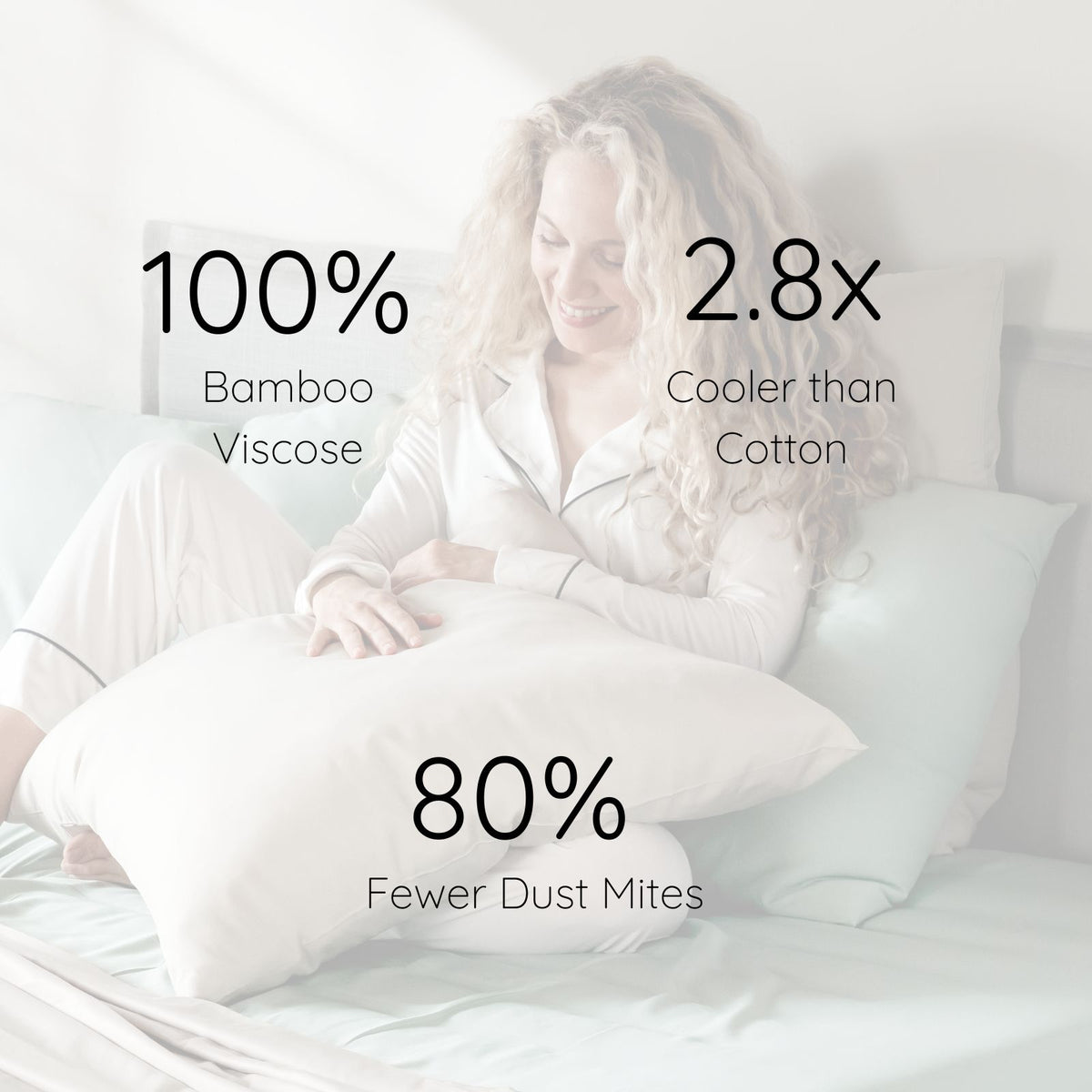A woman in light pajamas sits on a bed holding a large sand colour bamboo viscose pillow, with overlaid marketing text reading '100% Bamboo Viscose,' '2.8x Cooler than Cotton,' and '80% Fewer Dust Mites.