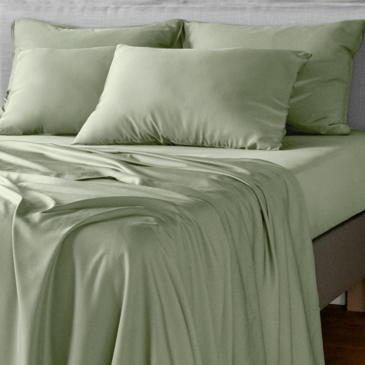 Light sage green bamboo bed sheets and matching pillowcases on a bed, shown in a clean, styled bedroom setting.