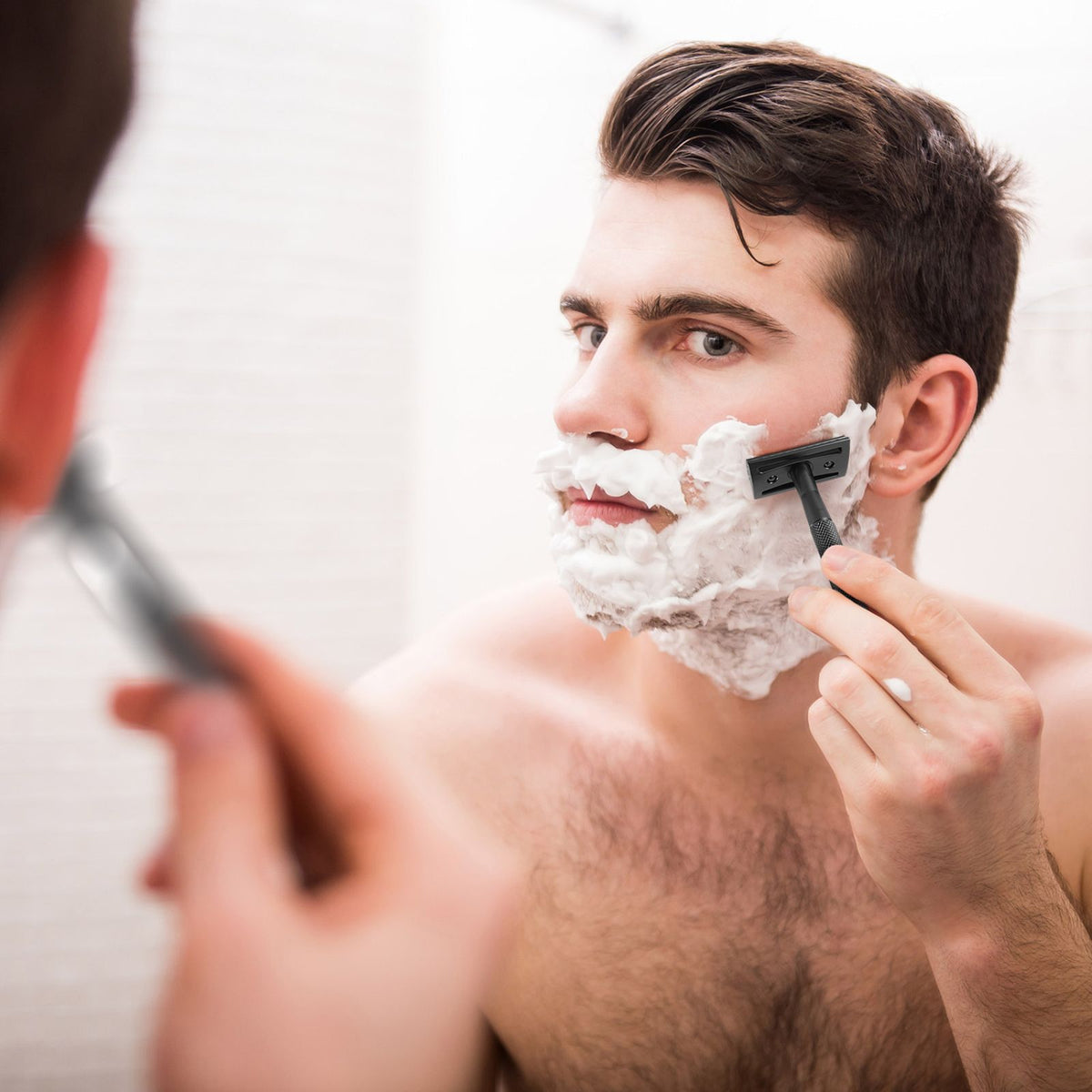 Man shaving his face with a Bambaw safety razor and shaving cream in front of a mirror.