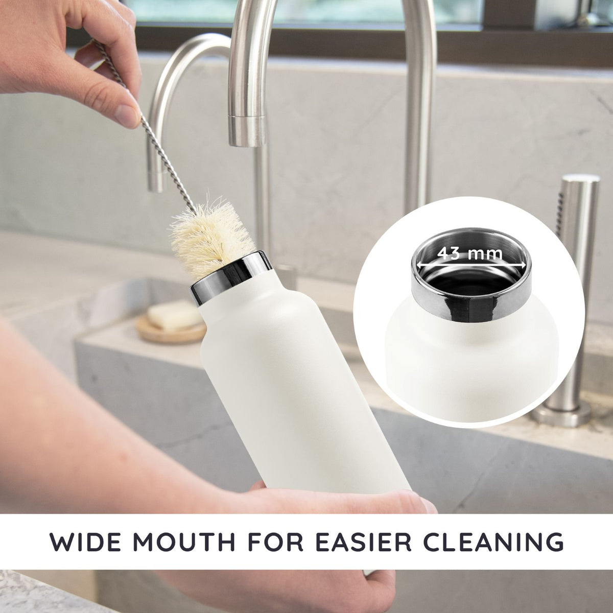 Person cleaning a bambaw wide mouth insulated bottle with a brush in a kitchen setting, emphasizing the wide mouth design.