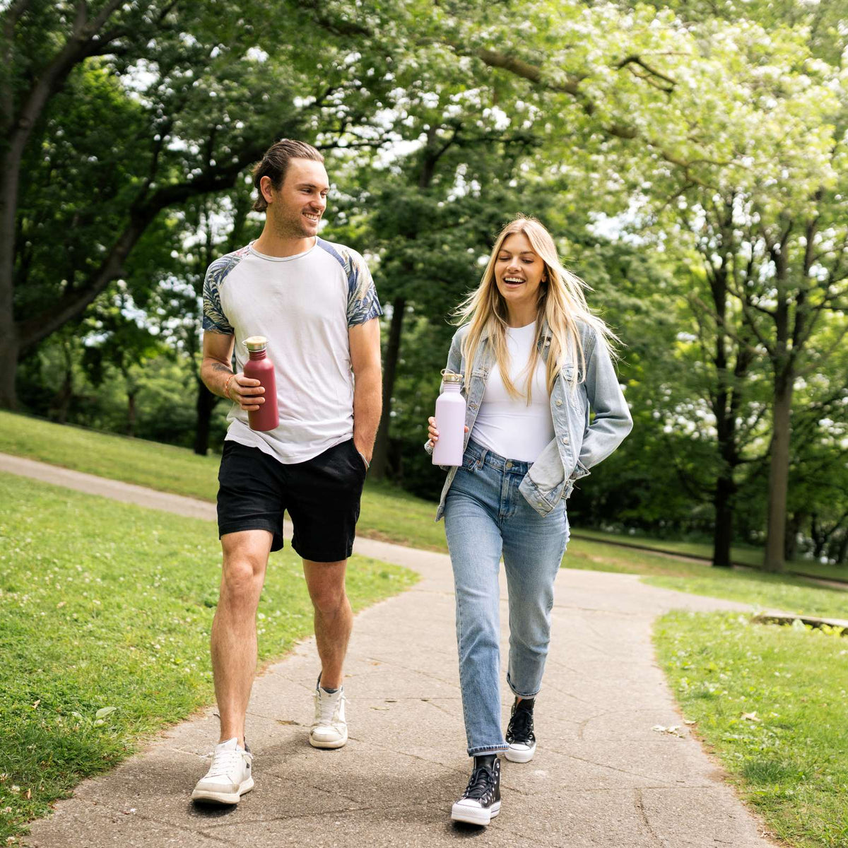 Two people walking on a path in a park holding bambaw reusable water bottles