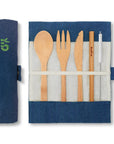 Open bamboo cutlery set arranged in a blue denim roll with five wooden utensils and a serrated blade.