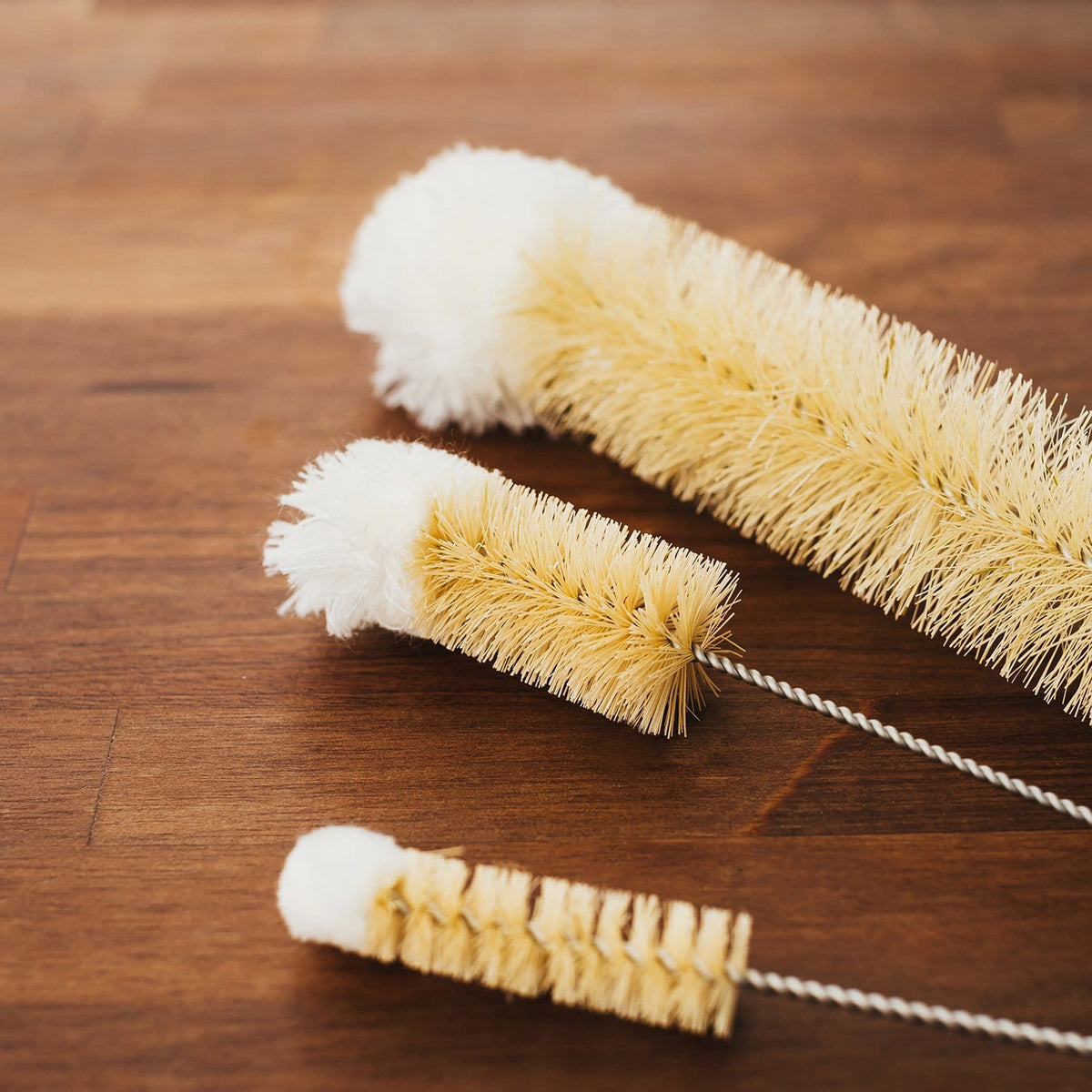 Close up of beige natural bristle bottle brushes on a wooden surface.