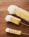 Close up of beige natural bristle bottle brushes on a wooden surface.