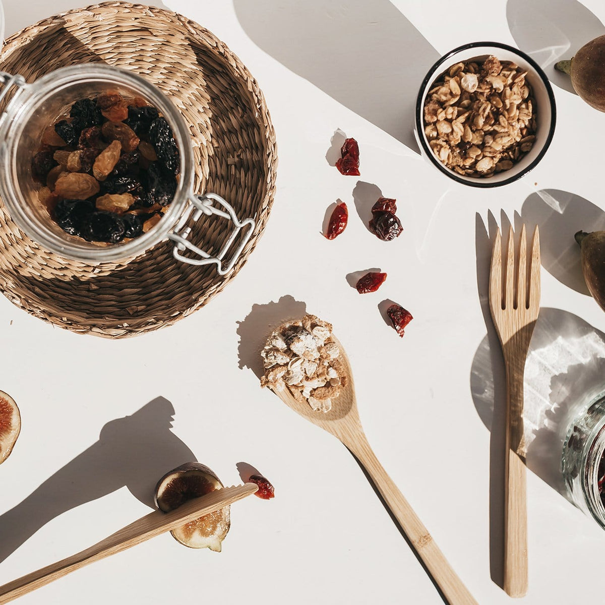 Overhead view of a bamboo cutlery set beside a jar of dried fruit and a bowl of oats on a white table