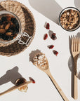 Overhead view of a bamboo cutlery set beside a jar of dried fruit and a bowl of oats on a white table