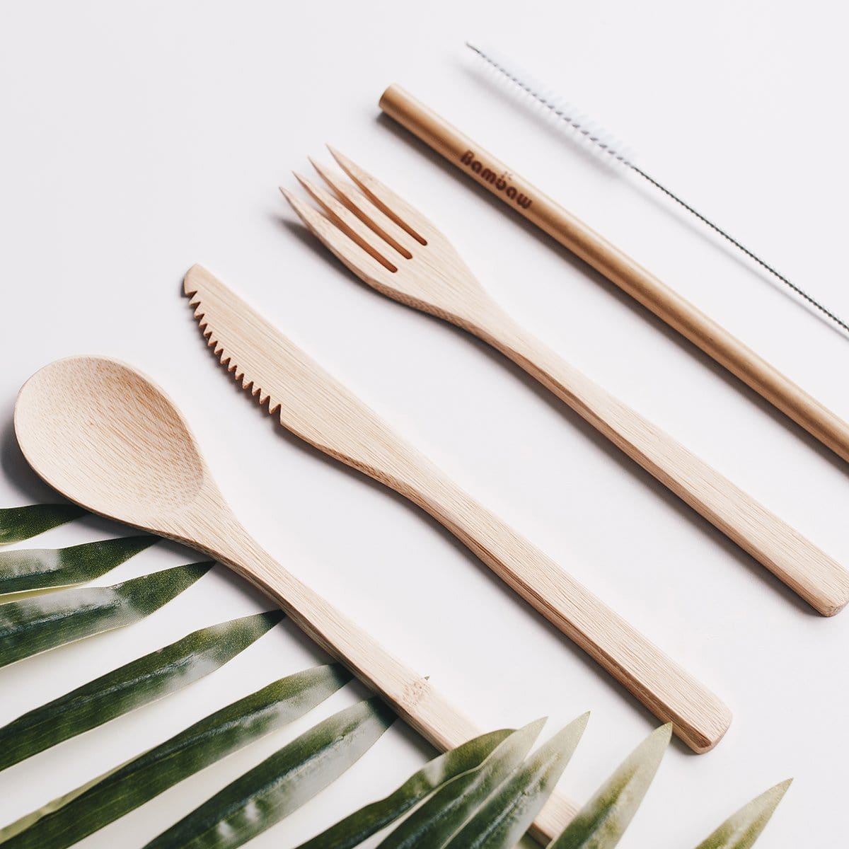 Flat lay of a natural bamboo cutlery set including spoon, fork, knife and chopsticks on a white surface