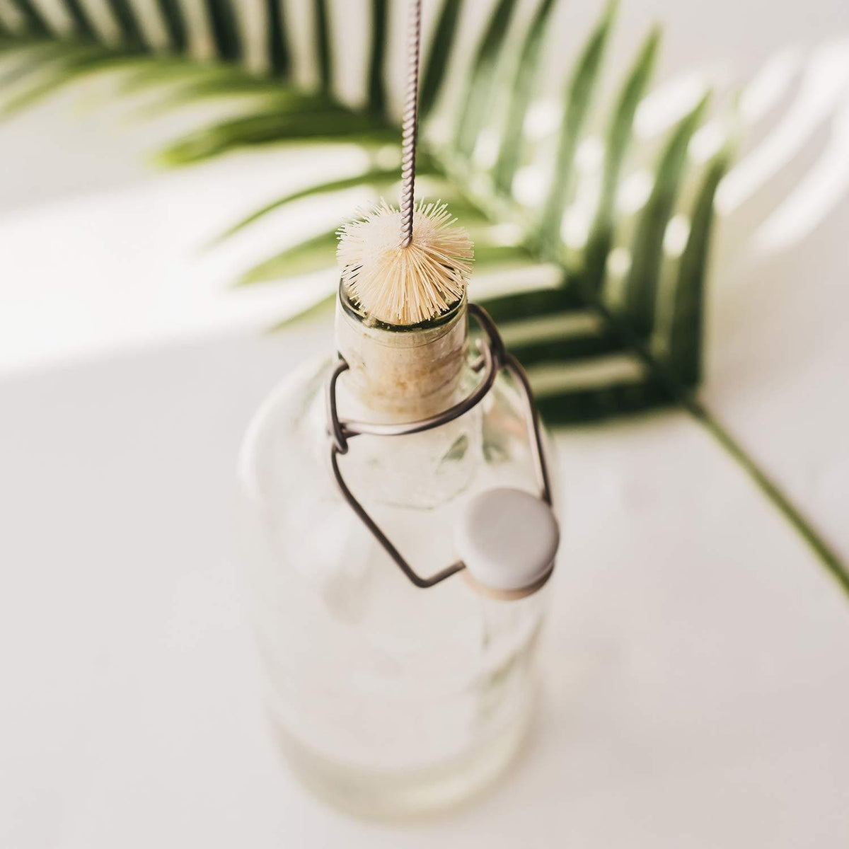 Beige circular bristle bottle brush perched on the mouth of a glass bottle with a hanging string