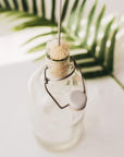Beige circular bristle bottle brush perched on the mouth of a glass bottle with a hanging string