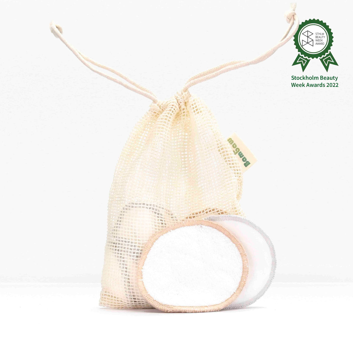 Beige reusable makeup remover pads in a mesh drawstring bag against a white background with an awards badge