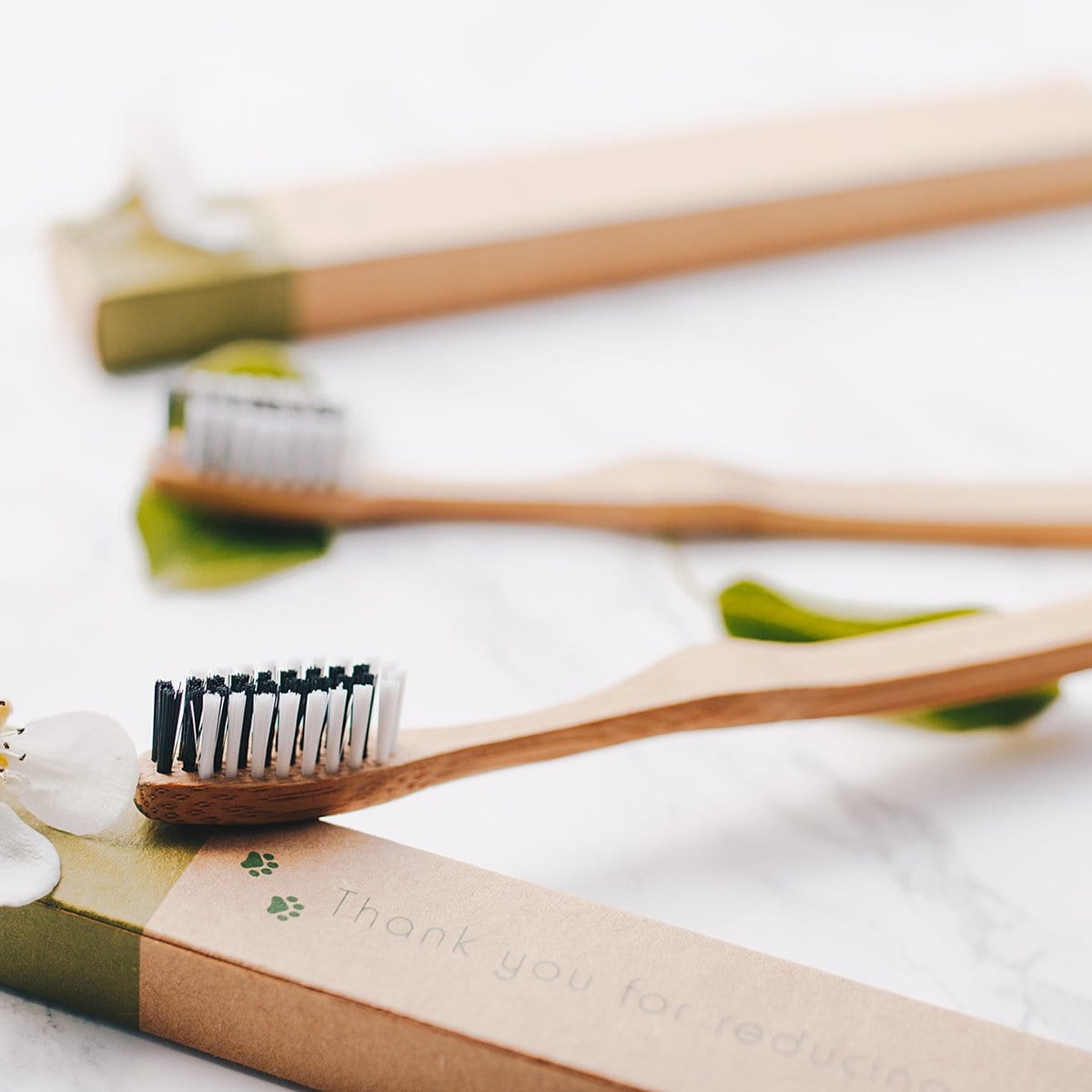 Close-up of a bamboo toothbrush on a marble surface with gift wrap and greenery