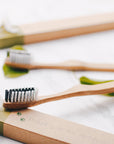 Close-up of a bamboo toothbrush on a marble surface with gift wrap and greenery