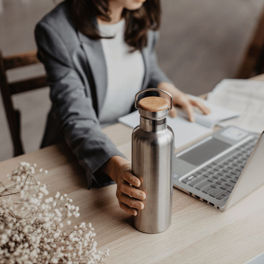 Person in a blazer sits at a desk holding a stainless steel insulated water bottle with a wooden cap.