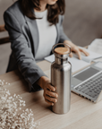 Person in a blazer sits at a desk holding a stainless steel insulated water bottle with a wooden cap.