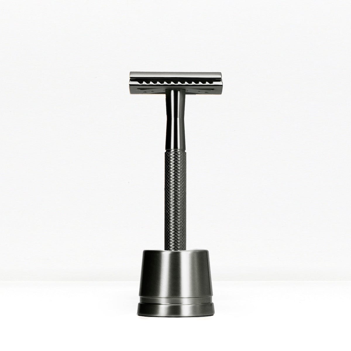 Black handled metal double edge razor on a dark stand against a white background