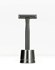 Black handled metal double edge razor on a dark stand against a white background