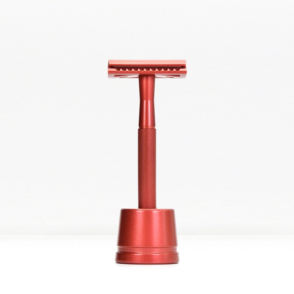 Red metal double edge razor with stand against a white background