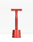 Red metal double edge razor with stand against a white background