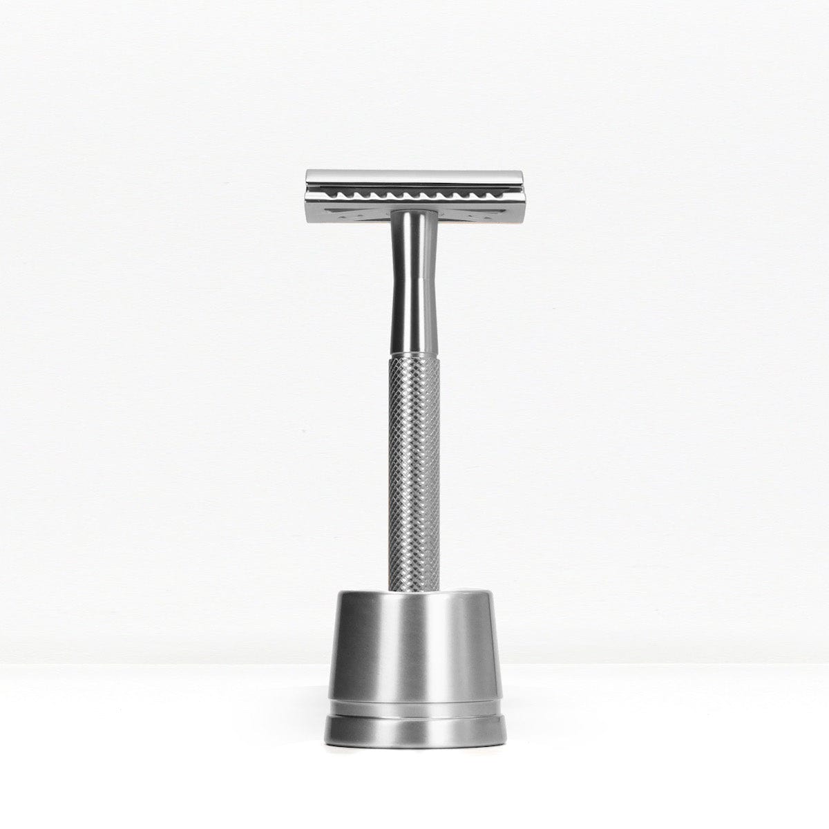 Silver metal double edge razor on a matching silver stand against a white background