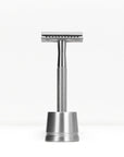 Silver metal double edge razor on a matching silver stand against a white background