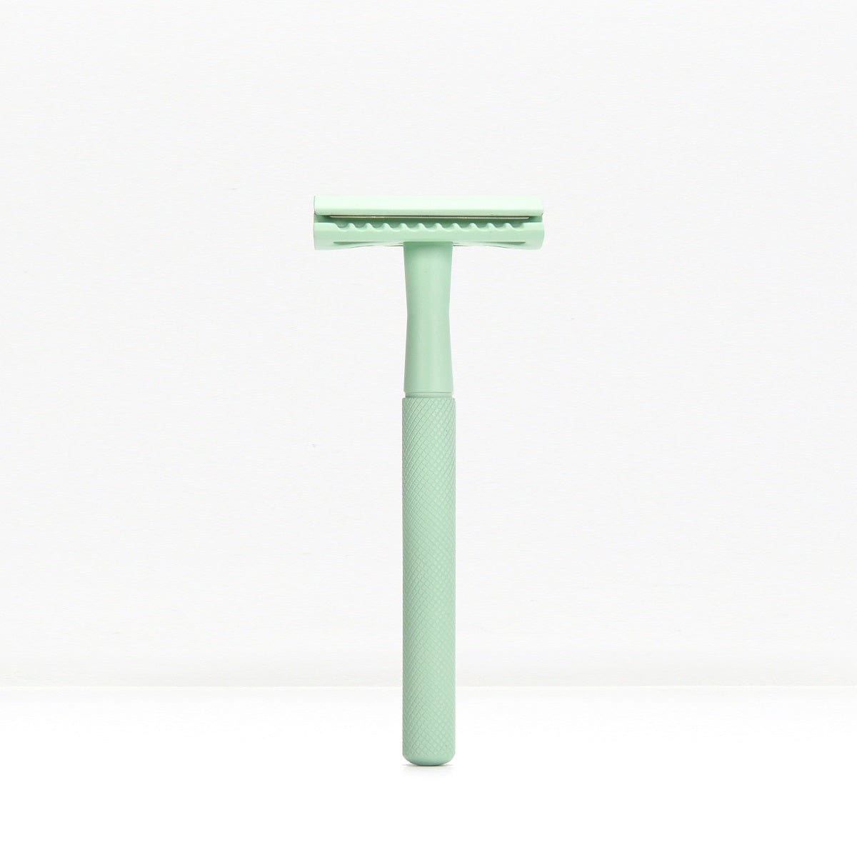 Mint green metal double edge safety razor with a knurled handle standing upright