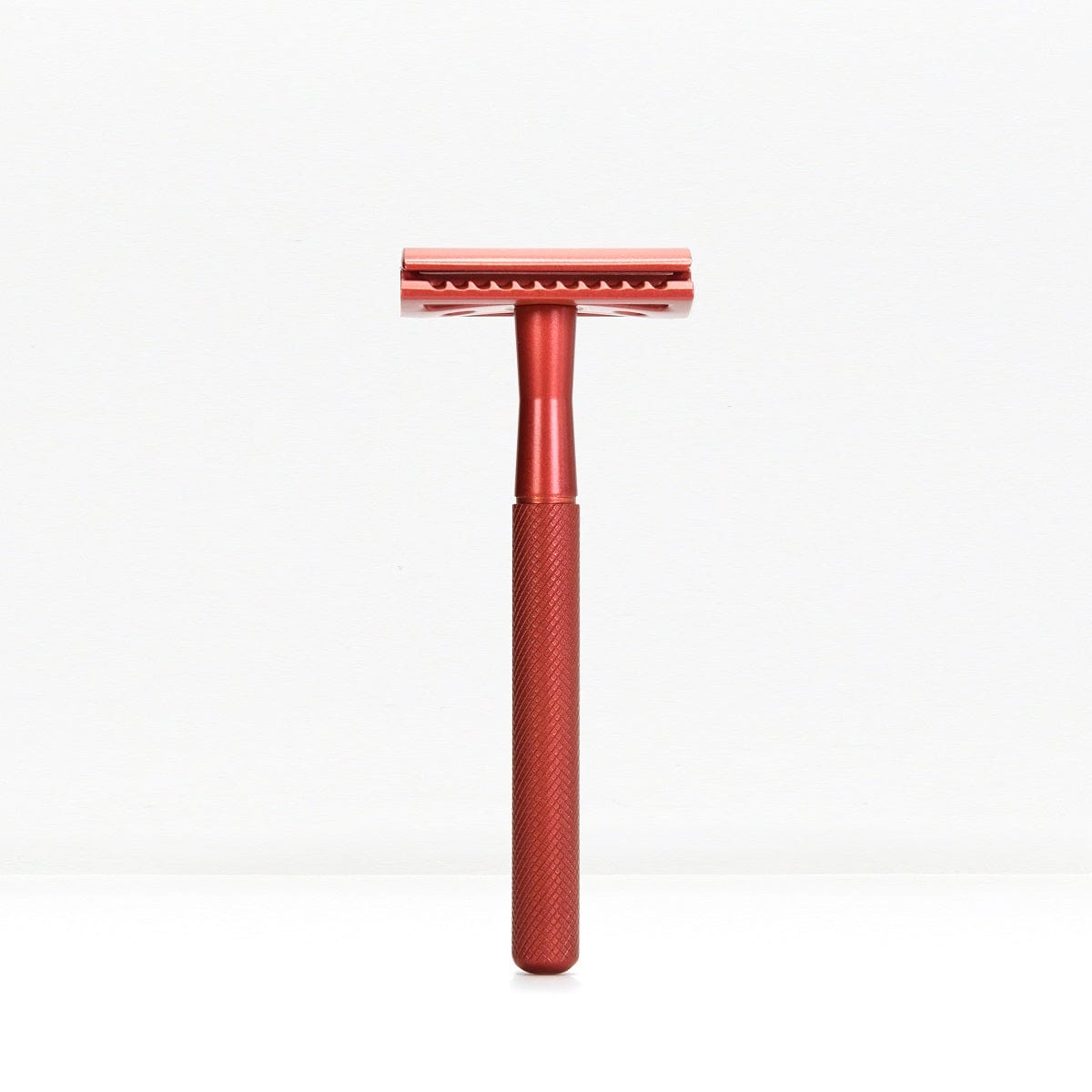 Red metal double edge safety razor with a knurled handle standing upright