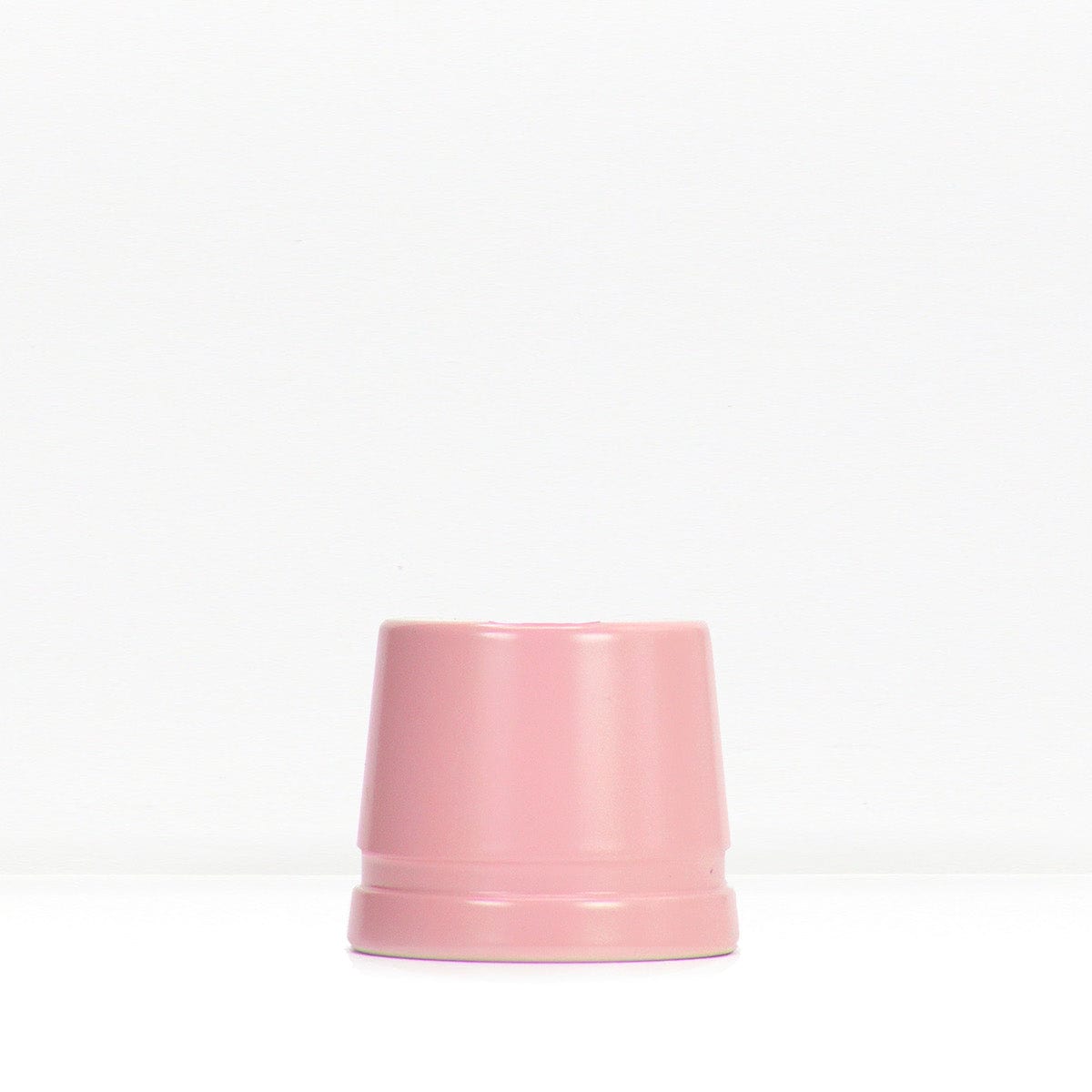 Soft pink metal safety razor stand resting on a white surface
