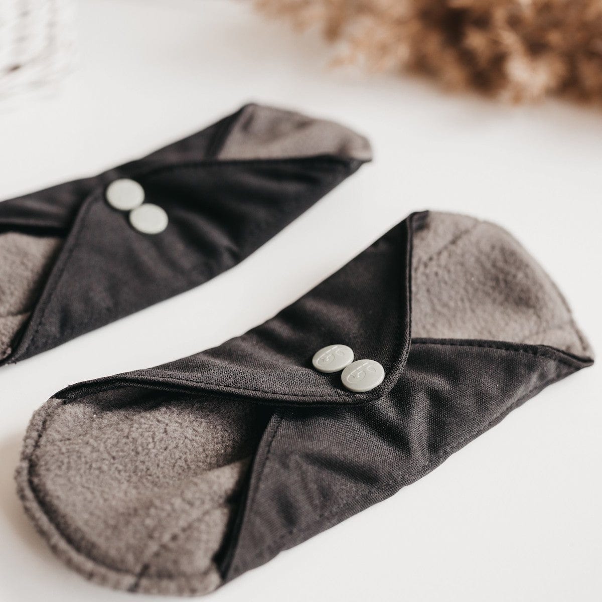 Close-up of two black reusable panty liners with gray interior and silver snaps.