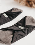 Close-up of two black reusable panty liners with gray interior and silver snaps.
