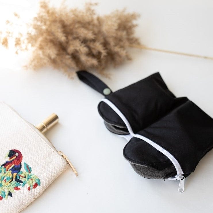 Single black reusable panty liner with gray lining on a white surface beside a decorative embroidered pouch.