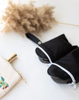 Single black reusable panty liner with gray lining on a white surface beside a decorative embroidered pouch.