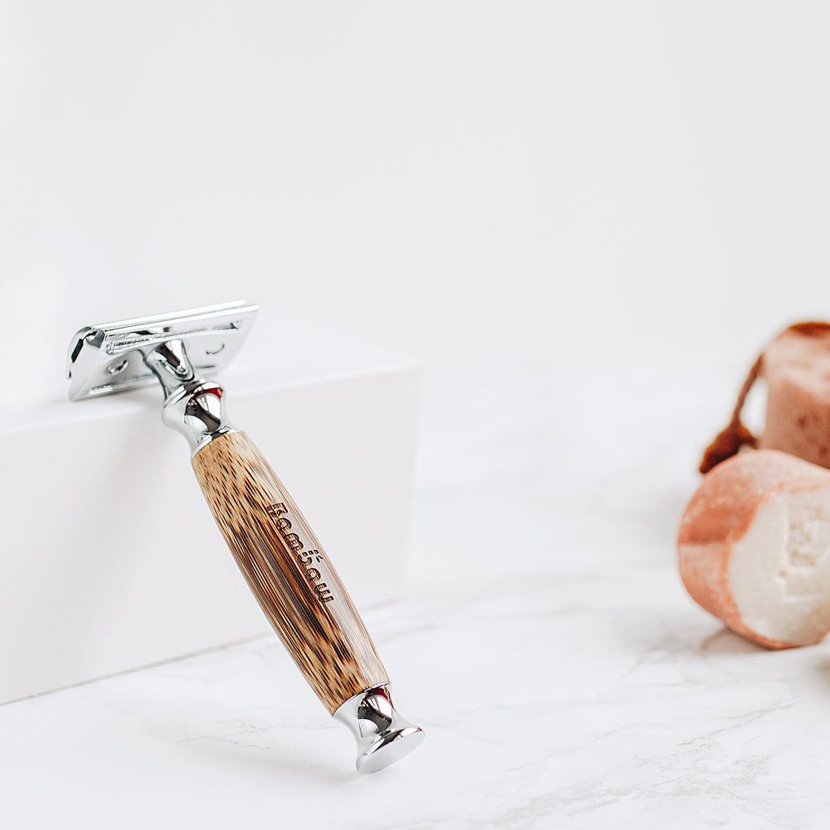 Close up of bamboo safety razor with wooden handle resting on a white marble surface