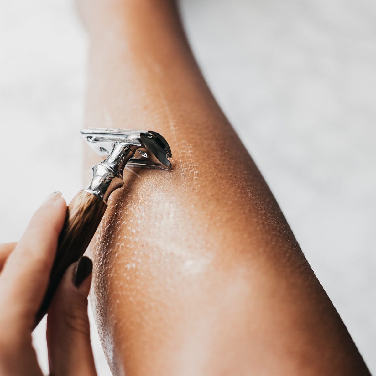 Close up of a bamboo safety razor gliding over a forearm with shaving foam.