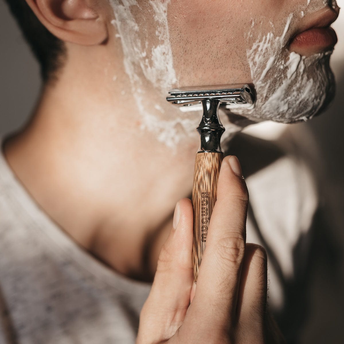Person shaving the jawline with a bamboo safety razor and foamy lather on the face.
