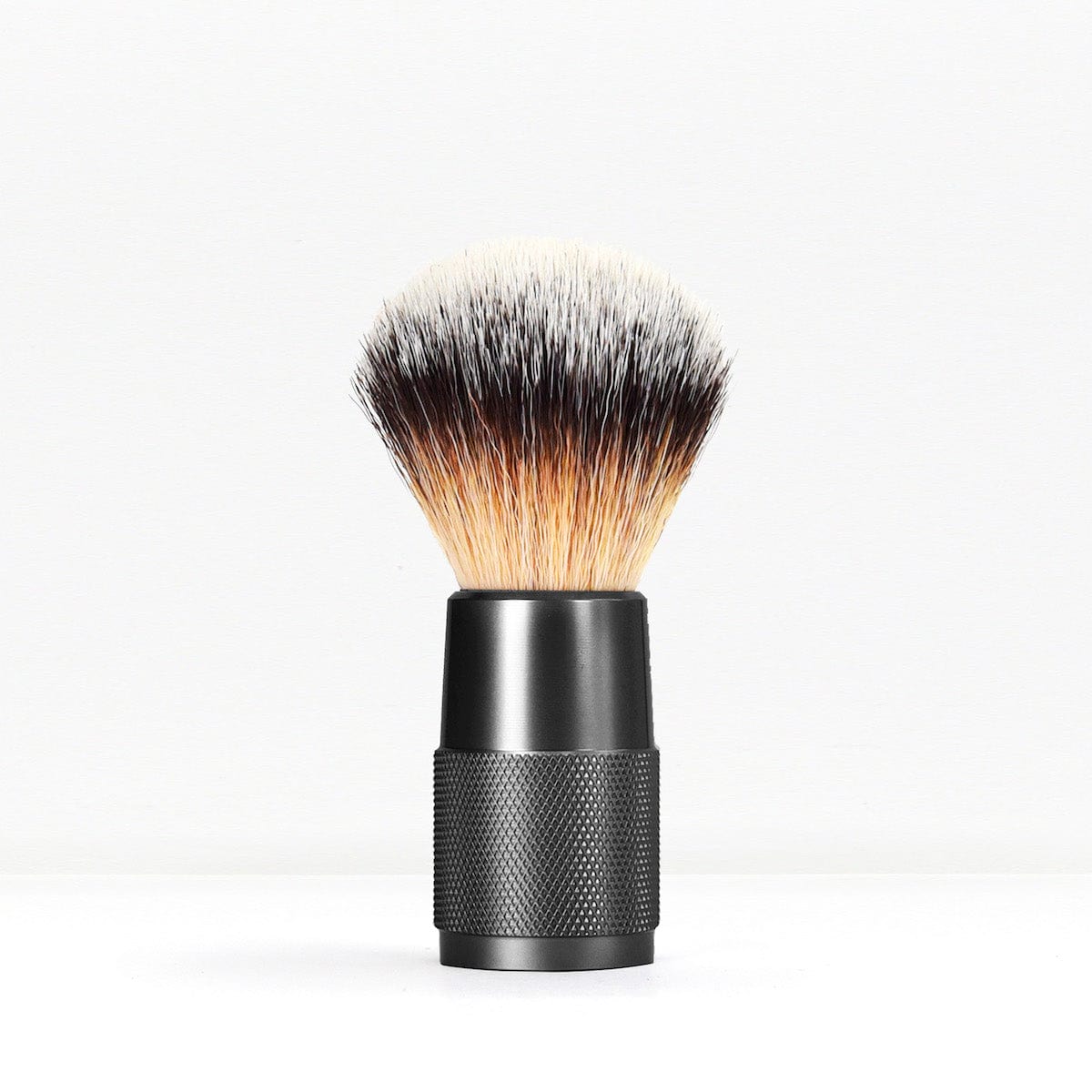 Shaving brush with a knurled black handle and dense light to dark bristles against a white background