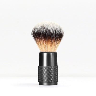 Shaving brush with a knurled black handle and dense light to dark bristles against a white background