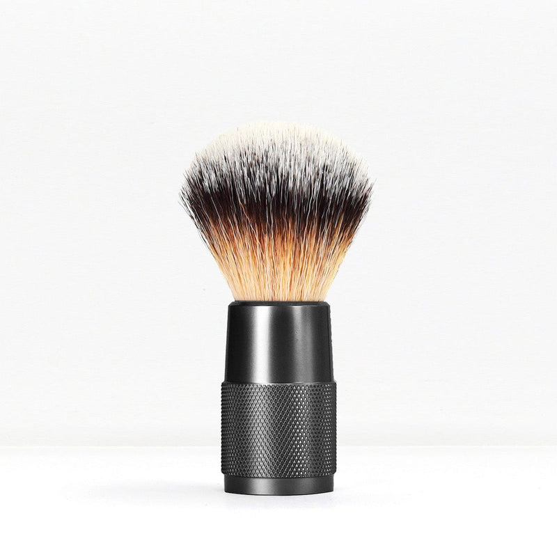 Shaving brush with a knurled black handle and dense light to dark bristles against a white background