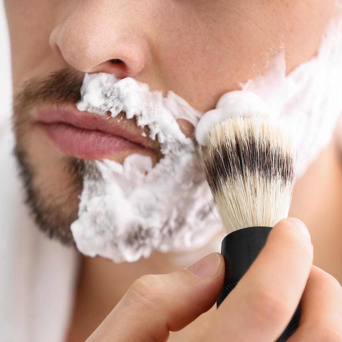 Close up of a man applying shaving foam with a brush to his cheek