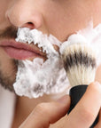 Close up of a man applying shaving foam with a brush to his cheek