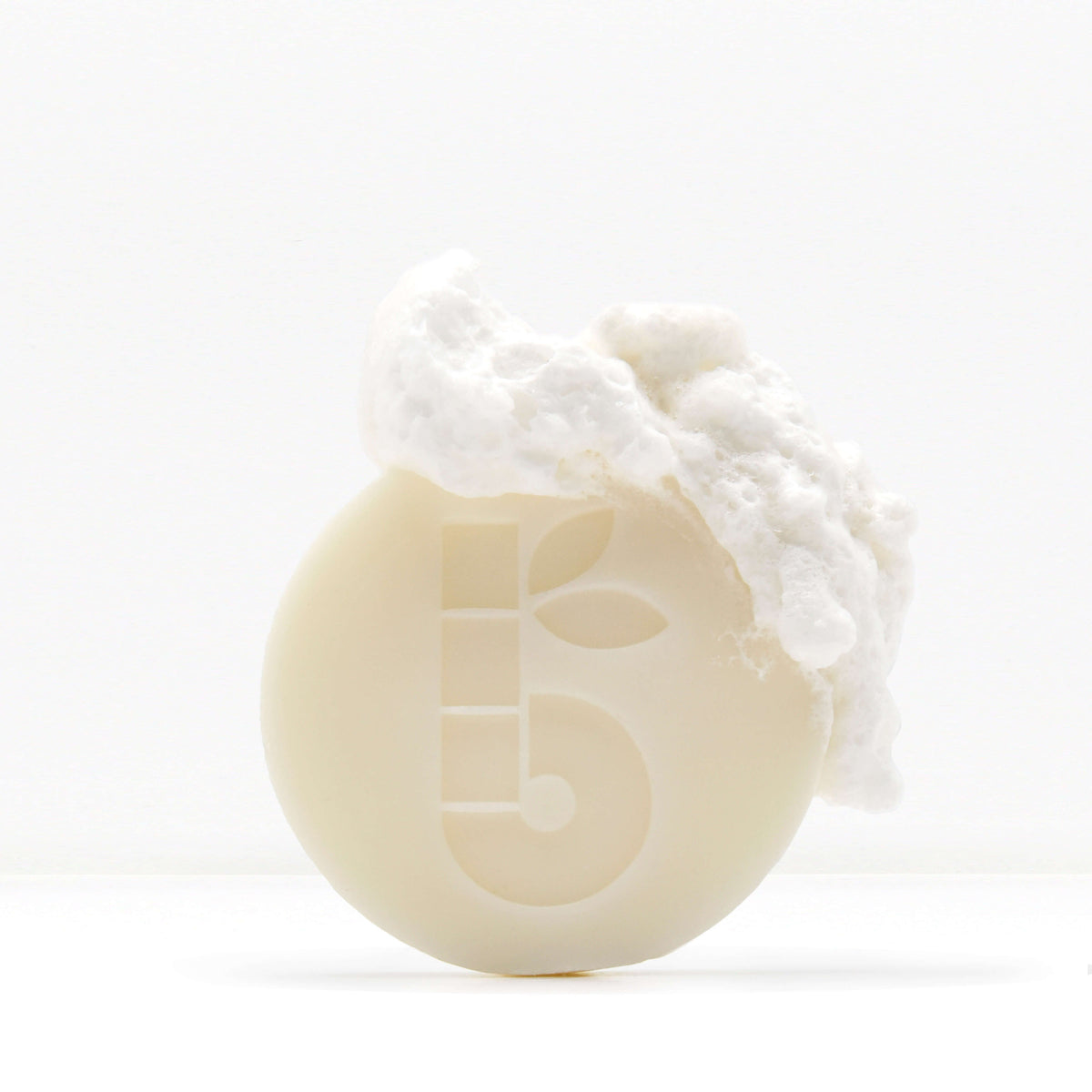 Close-up of a pale shaving bar with rough white chunks on top against a white backdrop