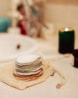 Stack of round reusable makeup remover pads resting on a beige mesh bag.