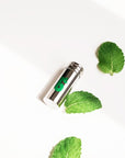 Shiny metal floss container with a green leaf graphic resting on its side on a white surface