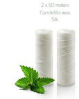 Two white silk floss spools beside mint leaves on Candellila wax Silk packaging